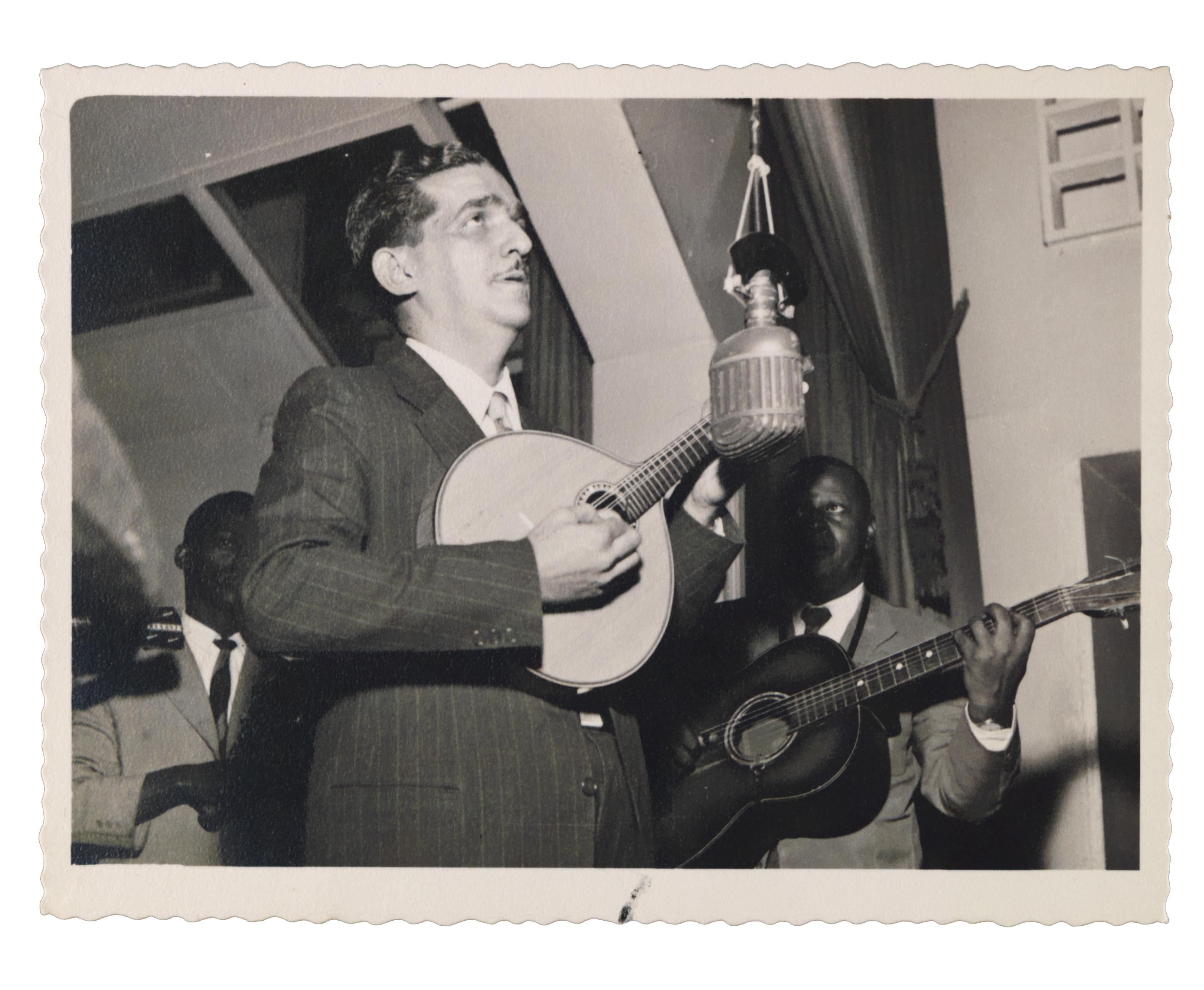 Jacob do Bandolim toca seu instrumento musical em emissora de rádio, próximo ao microfone e homens não identificados, 1930 - 
          Fotógrafo não identificado - 
          Coleção Jacob do Bandolim - 
          Acervo FMIS/RJ